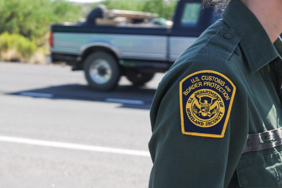 shoulder of a uniformed border patrol agent in front of a pickup truck