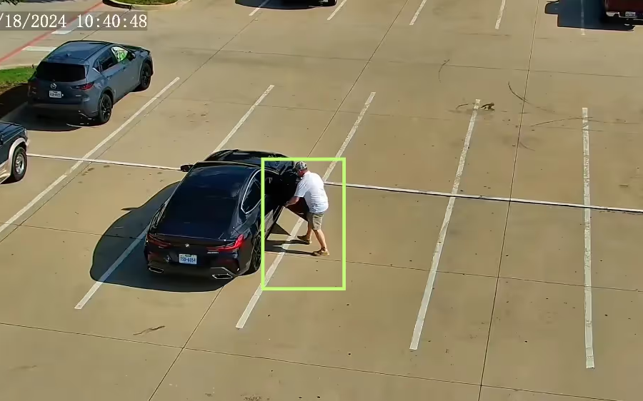 Flock generated surveillance video still. Guy opening a car door with a green targeting box around him