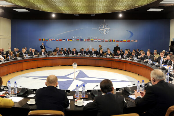 Large oval meeting room with NATO compass logo on the floor and lots of ministers and officials sitting around the circle.
